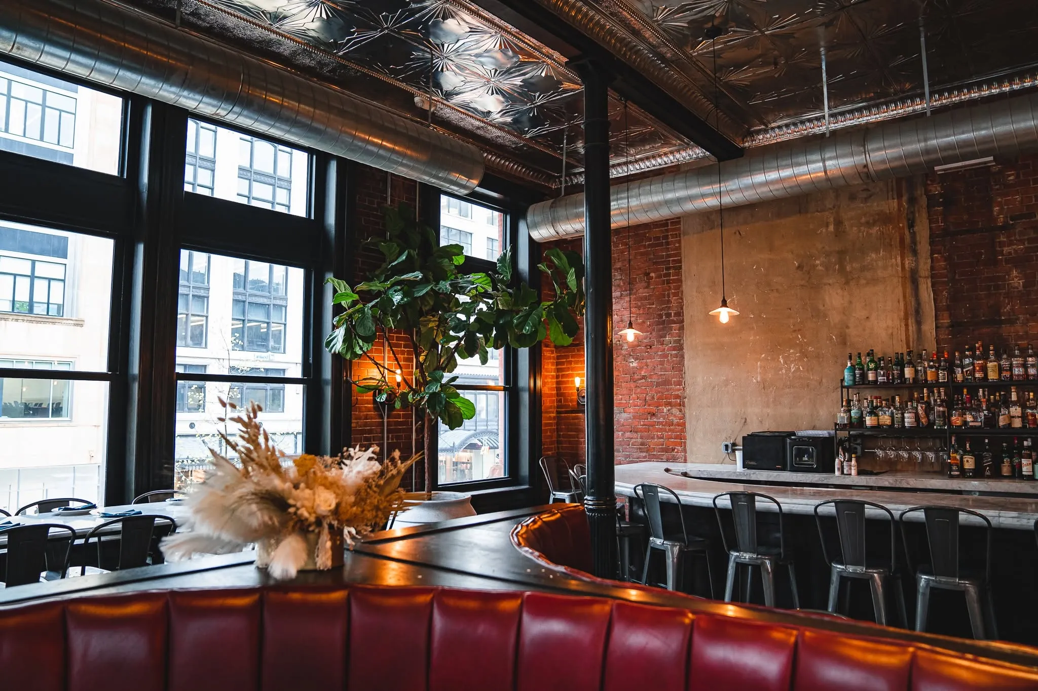 The Wright and Company dining room: red leather booths, a marble bar with metal stools, exposed brick, and tall windows over Woodward Avenue