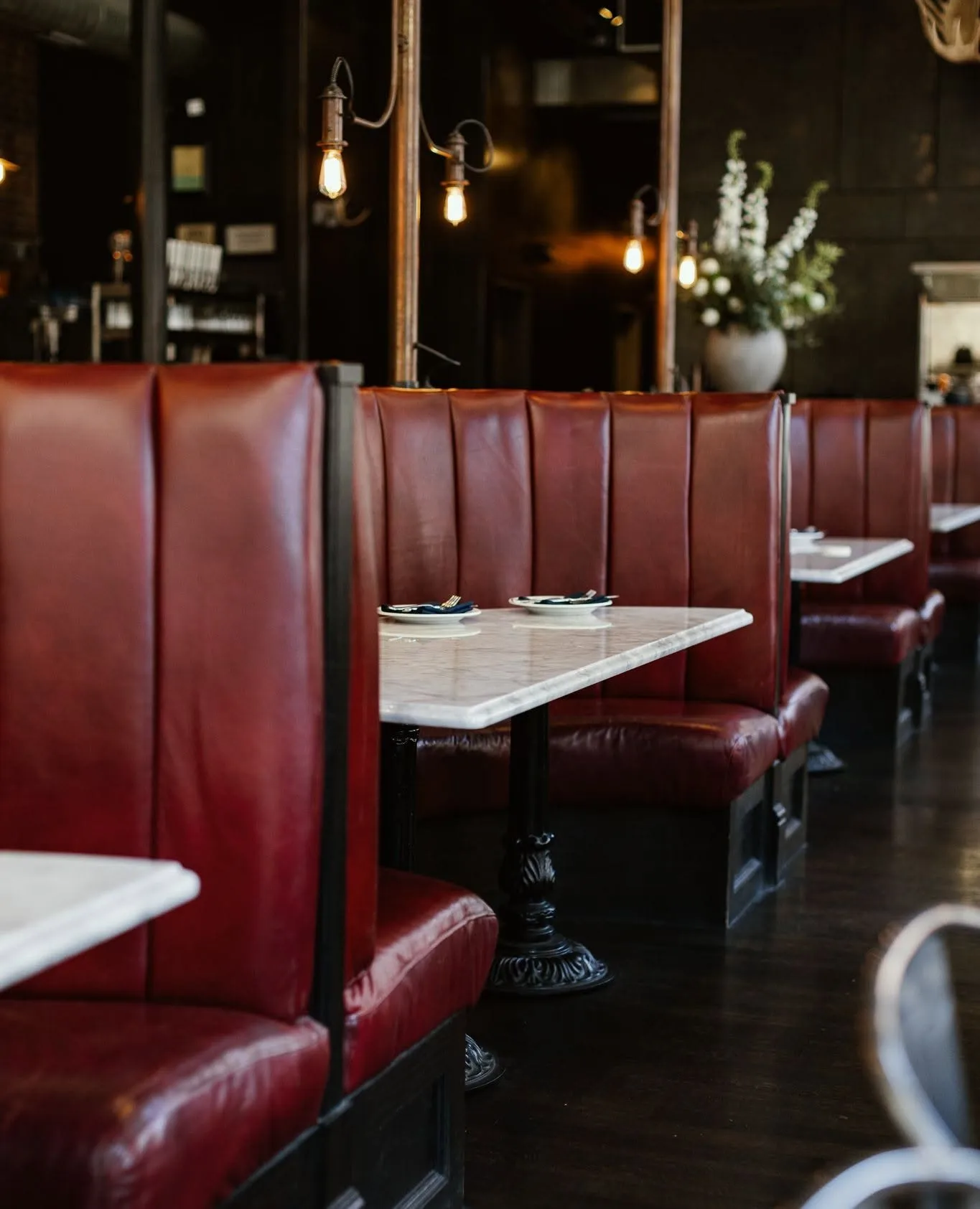 A row of deep red leather booths with marble tables and Edison lights at Wright and Company