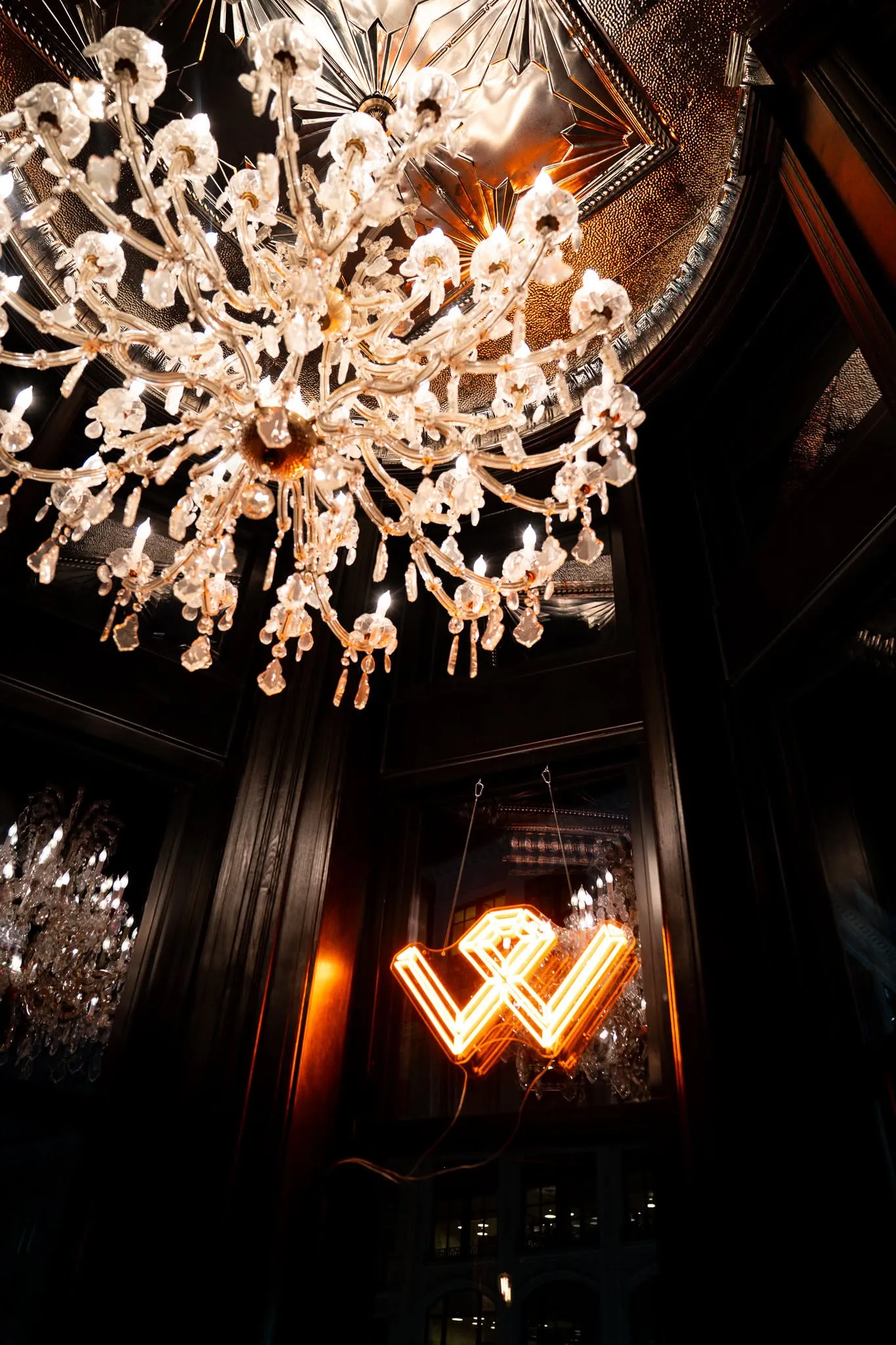 The crystal chandelier and the glowing neon Wright monogram beneath the pressed-tin ceiling at Wright and Company