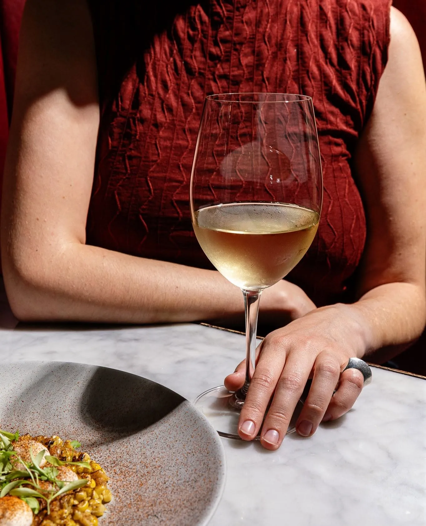 A guest holding a glass of white wine at the marble table at Wright & Company, a plated dish alongside