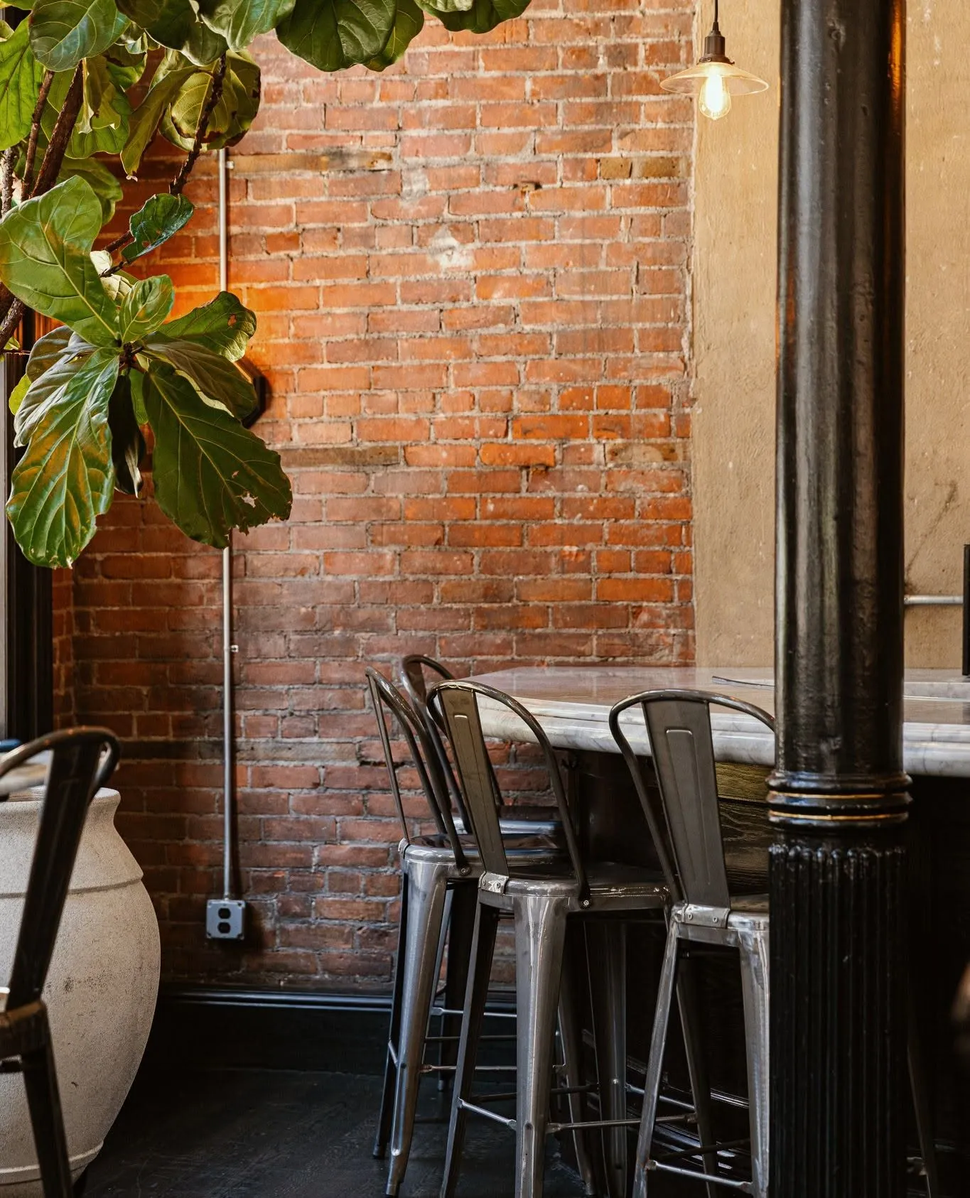 A marble high-top and industrial stools against the exposed brick wall at Wright & Company